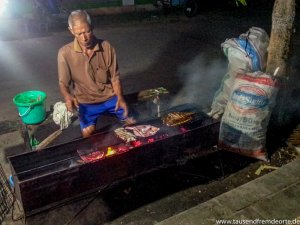 Mann vor einem Grill auf dem Fischmarkt auf Karimunjawa